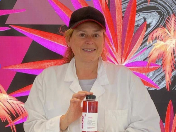 Dr. Sybille Buchwald-Wernerin white coat holding a red bottle with vibrant leaf backdrop