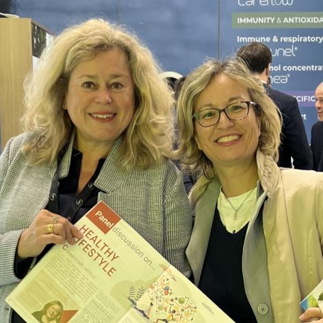 Two women smiling while holding a healthy lifestyle brochure at a wellness event